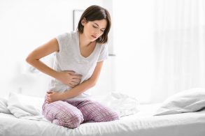 ベッドの上で腹痛をこらえる女性