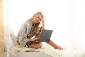ベッドの上でノートPCをいじる女性