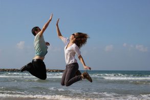海辺でジャンプハイタッチする男女